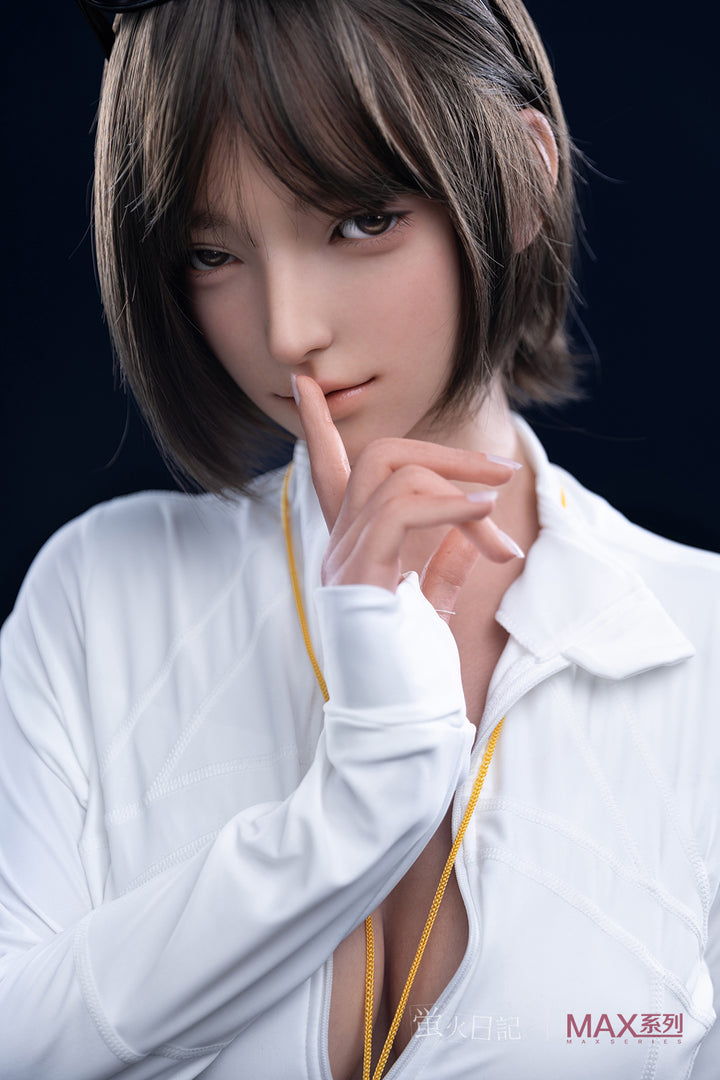 Realistic silicone doll with short brown hair and soft facial features, wearing a white long-sleeve blouse, holding a finger to her lips in a shushing gesture.