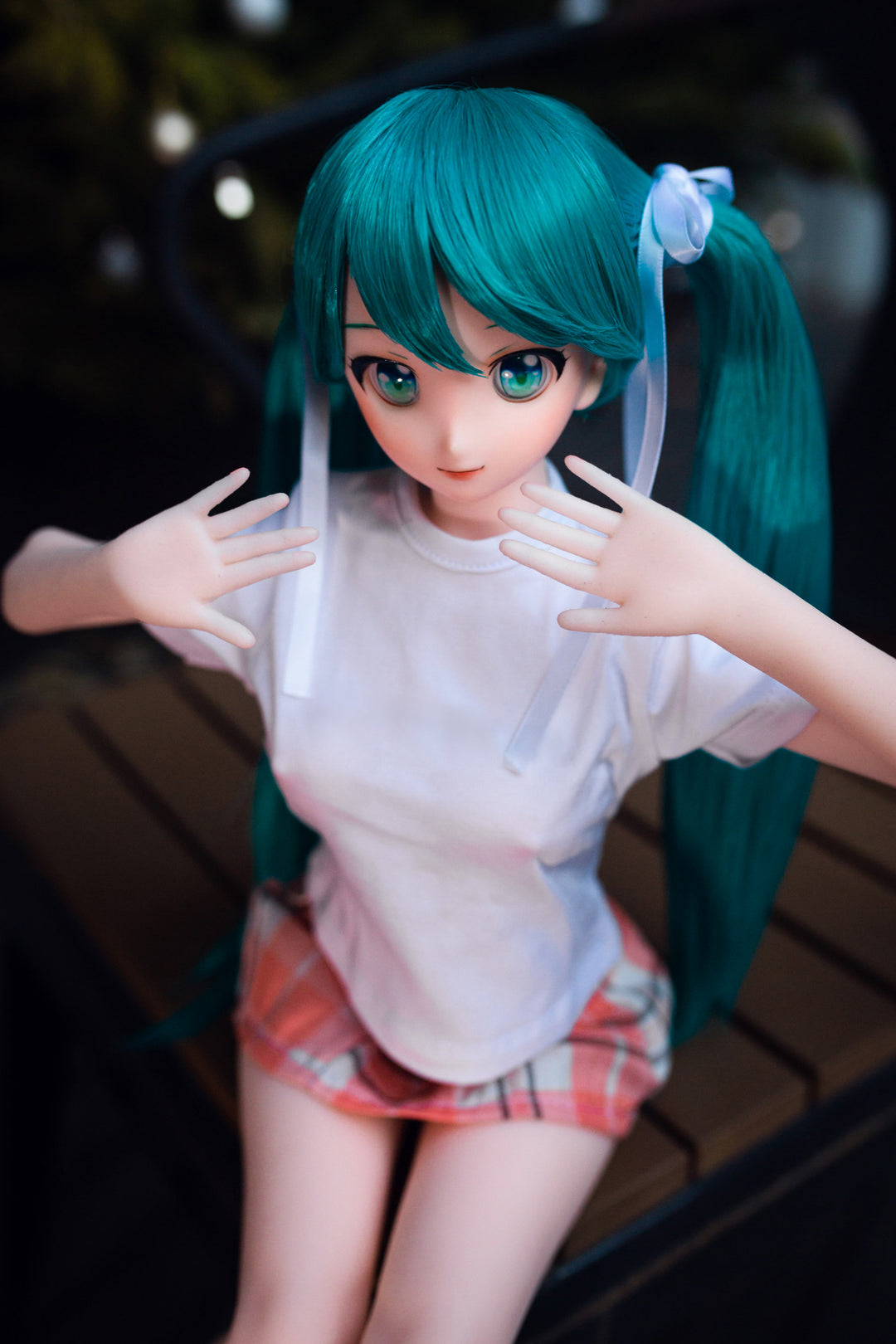 CLIMAX DOLL Mini J60 cm Hybrid - Miku (Cinnamon) - Seated on a dark wooden bench, leaning forward with hands on her knees, teal twin tails, white tee, pink plaid skirt, night garden with fairy lights.
