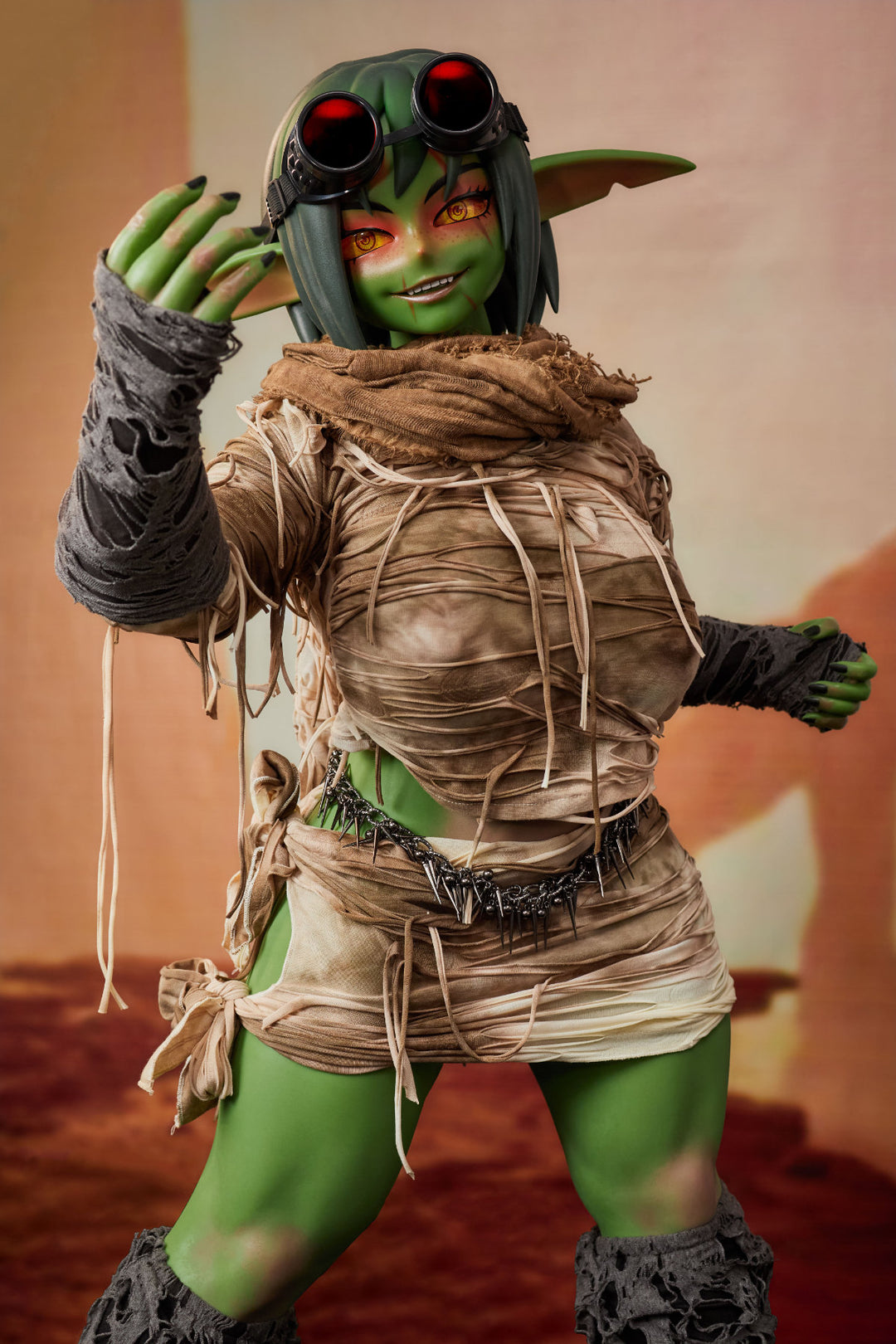 CLIMAX DOLL ULW SiF120 cm Silicone - Barza (Green) full body standing pose in tattered tan wrap outfit with raised hand, short green hair, desert red background
