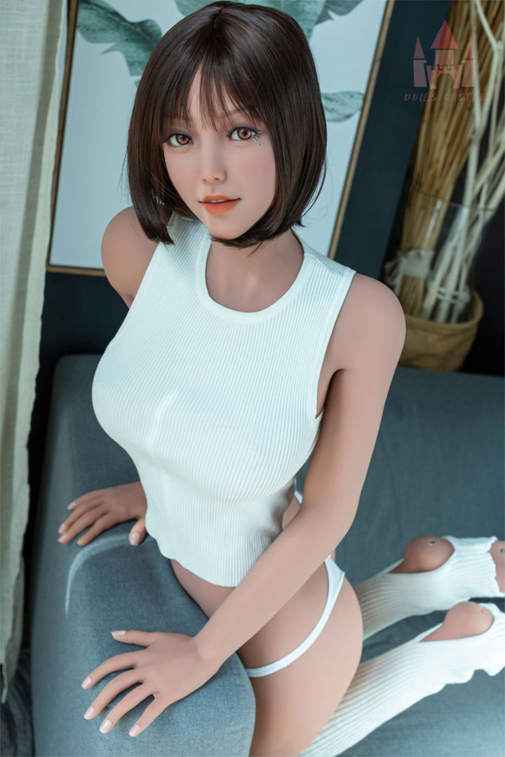 Dolls Castle® 163 cm E TPE - #K3 seated pose in white sleeveless top and white shorts, short brown bob hair, teal indoor background
