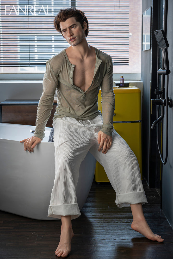 FANREAL DOLL 173 CM Silicone - Male Carter V2 sitting on a bathtub in a bathroom wearing a beige shirt and white pants.