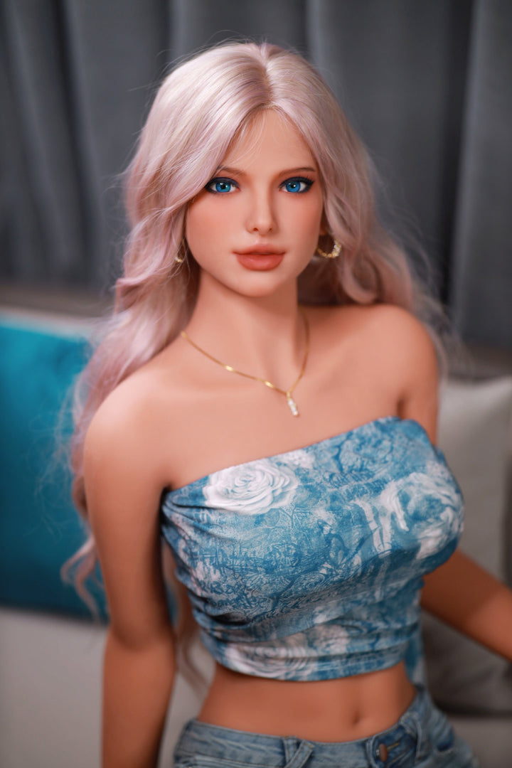 Fire Doll 166 cm C TPE - Flora close-up upper body shot in blue floral denim tube top with gold necklace, long pink-blonde wavy hair, bright indoor background
