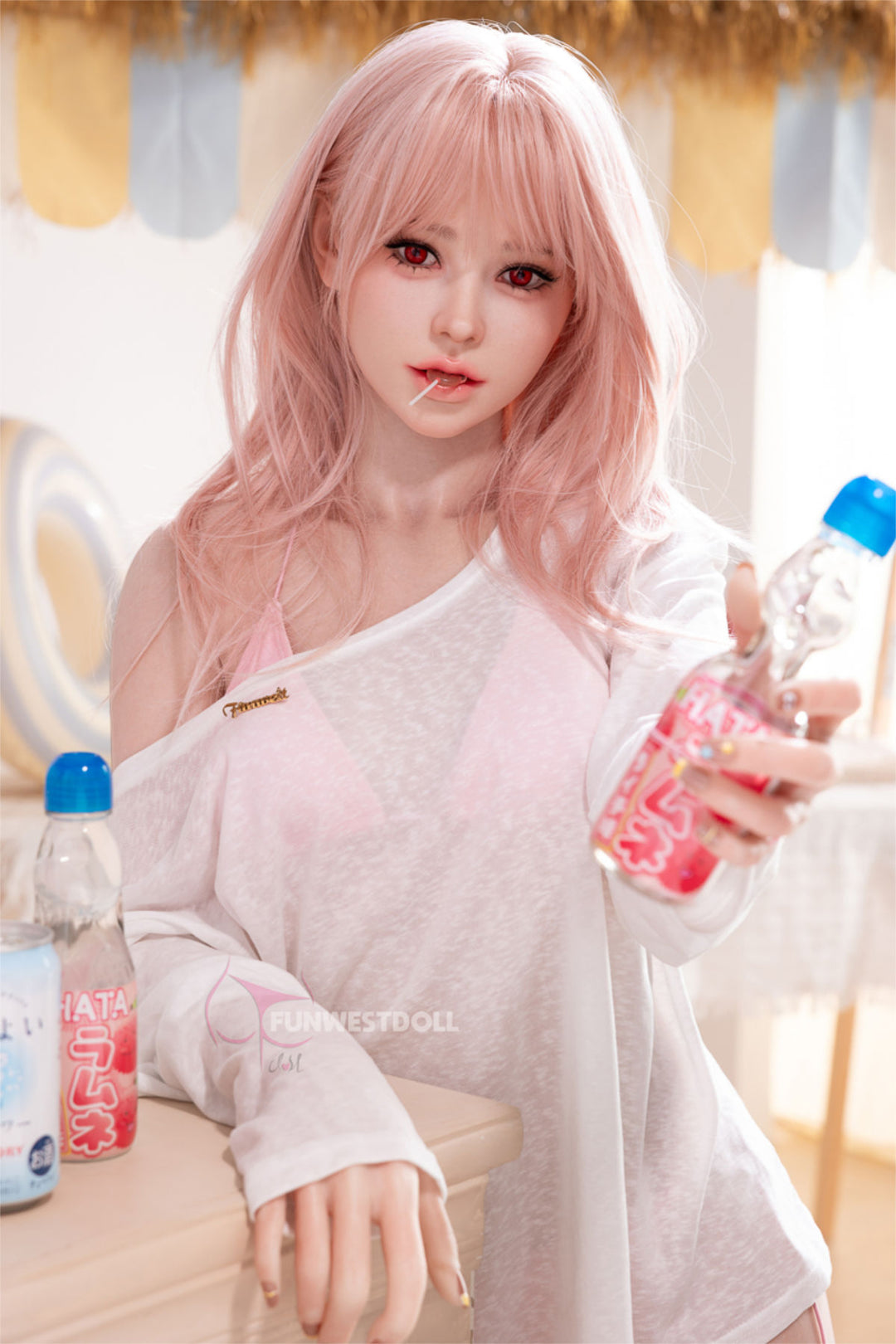 FunWest Doll 159 cm A Silicone - Lucy (Real Skin Texture) seated at a wooden table, wavy rose-pink hair with soft bangs, holding a blue water bottle, sheer white blouse slipping off one shoulder, cozy indoor setting with a blue curtain backdrop