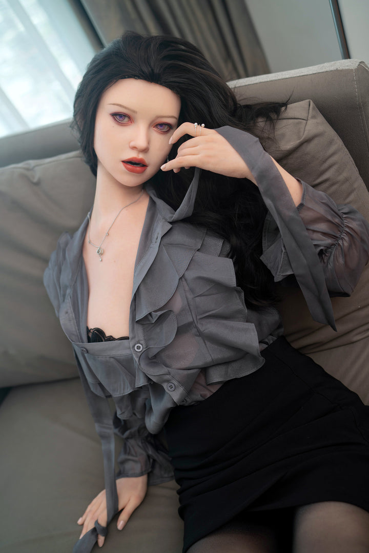 Zelex Inspiration Series 165 cm F-cup silicone sex doll – GE64-1 seated on sofa, dressed in sheer grey ruffled blouse and black skirt, realistic face and soft makeup