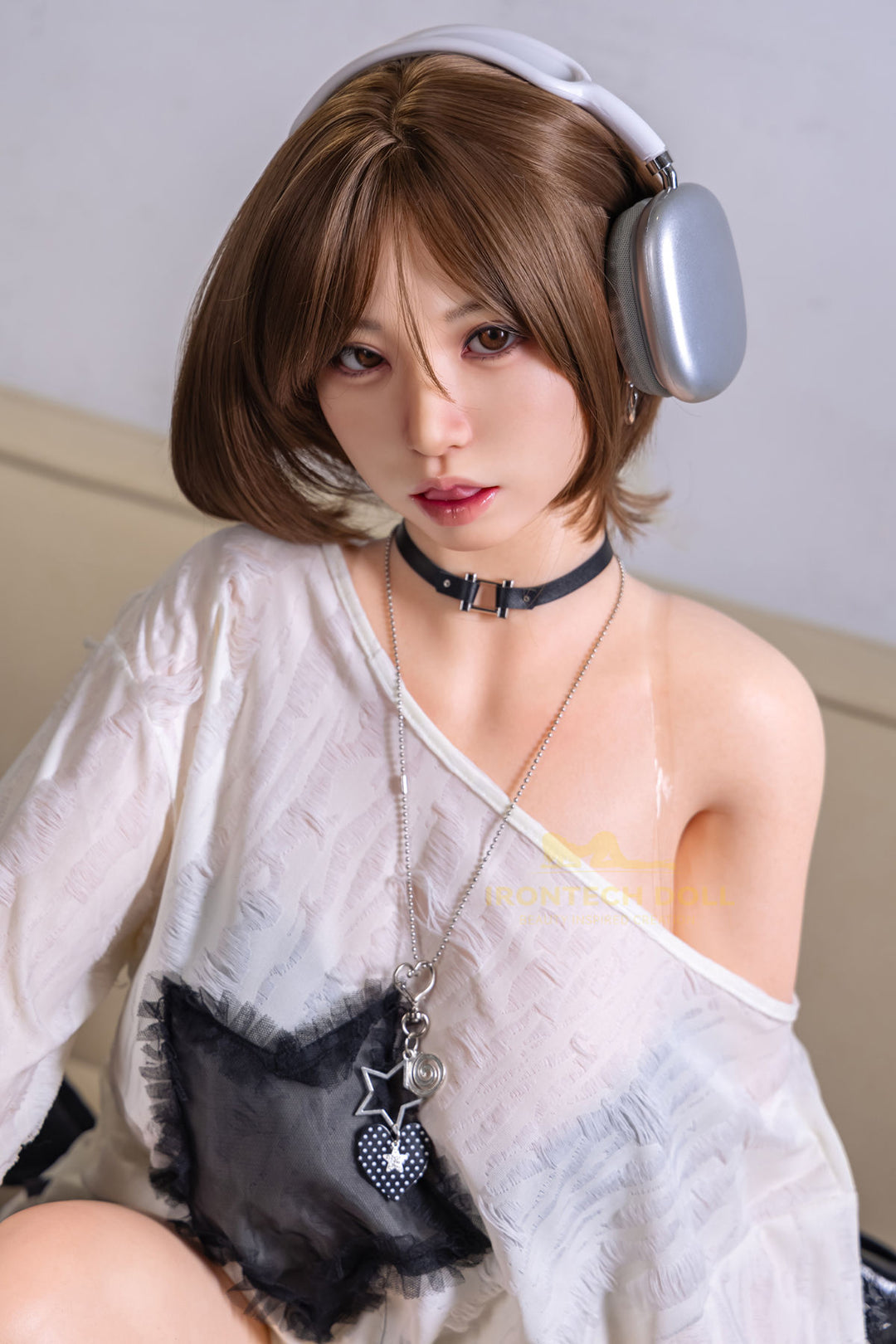 Irontech 165T F Silicone - Suki V2 close-up portrait, short wavy chestnut brown bob, over-ear headphones, black choker, white oversized top slipping off one shoulder, black heart-shaped bag, soft gray studio backdrop