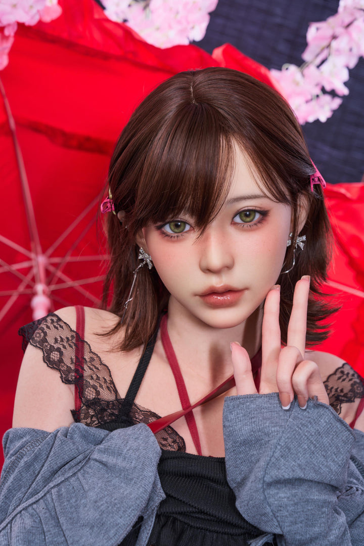 Close-up portrait of the Irontech Doll 151 cm D Oriental Series Silicone – Yuna with dark hair and bangs, wearing a grey off-the-shoulder cardigan and black lace top against a backdrop of cherry blossoms and a red umbrella.