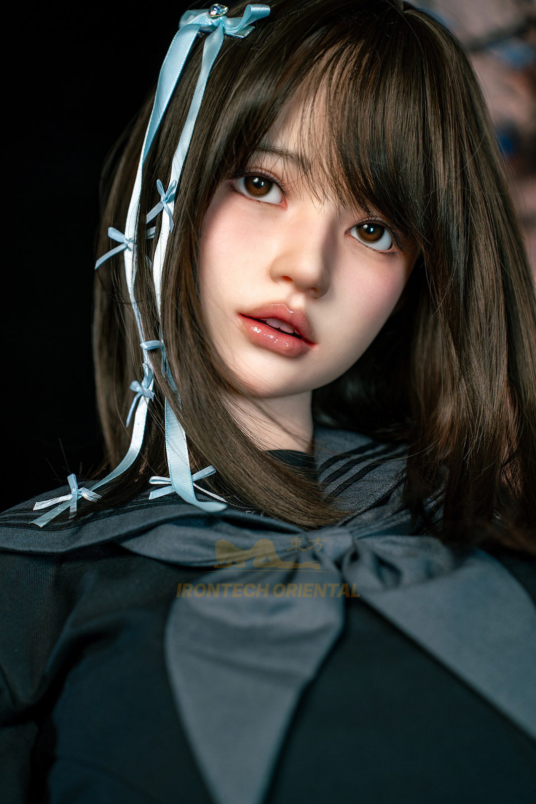 Irontech Doll 161cm F Oriental Series Silicone – Evie V4 – Standing pose, black kimono-style top with grey obi belt, blue hair ribbons, dark braided hairstyle, traditional wooden interior backdrop.