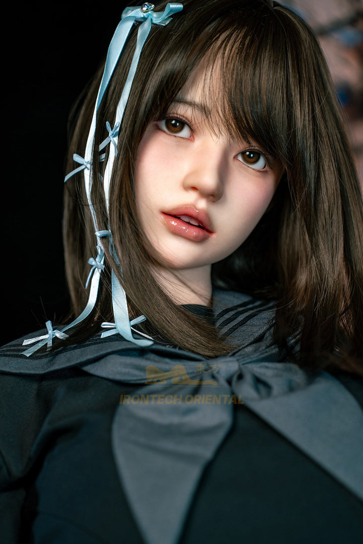 Irontech Doll 161cm F Oriental Series Silicone – Evie V4 – Standing pose, black kimono-style top with grey obi belt, blue hair ribbons, dark braided hairstyle, traditional wooden interior backdrop.
