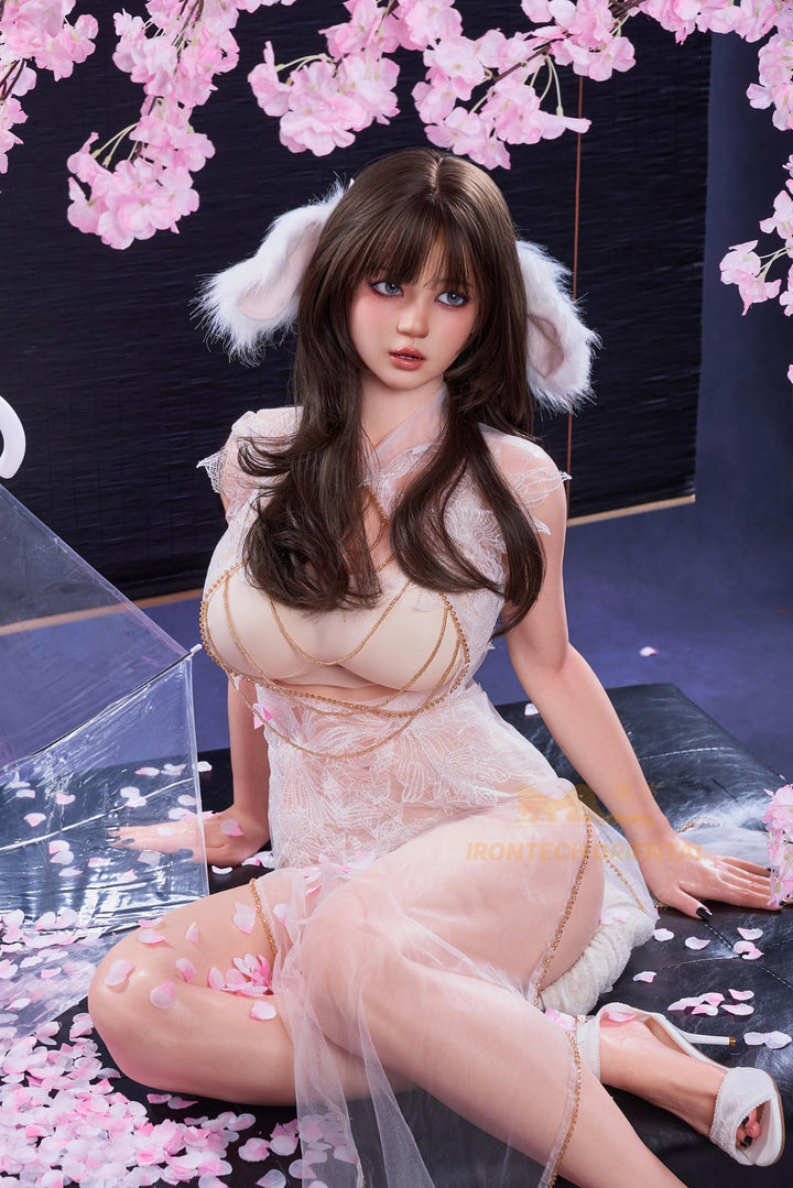 Irontech Doll 161 CM F Oriental Series Silicone - Nia V2 seated floor pose in sheer white outfit with cherry blossom background, side-angle view
