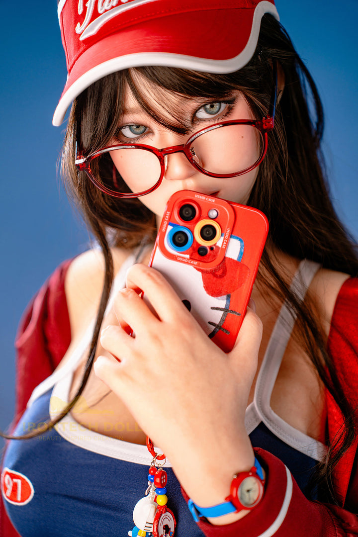 Irontech Doll 161 CM F Silicone - Evie close-up upper body view in blue top with red cap and glasses accessory, highlighting realistic facial features and skin texture against blue background