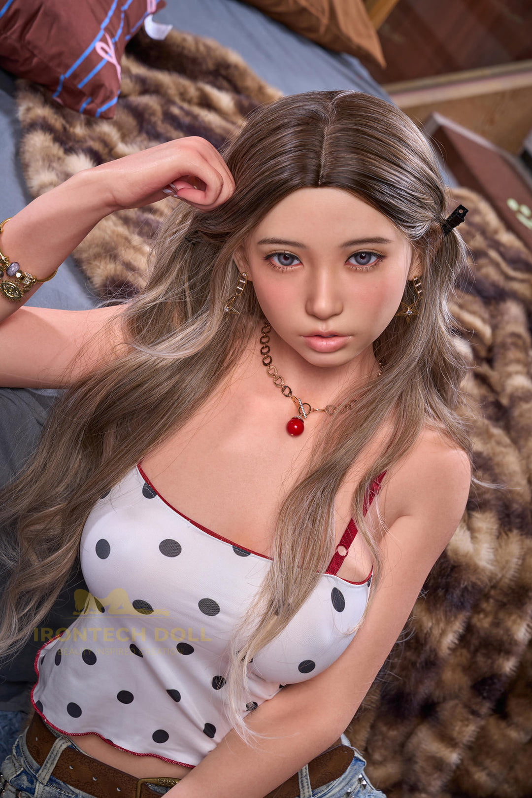 Irontech Doll 166 cm 2.0 E Silicone - Suki standing pose with one hand raised near her shoulder, wavy chestnut brown hair, white polka-dot crop top, layered necklaces with a red heart pendant, denim shorts, leopard-print throw over her shoulder, rustic wood cabin backdrop