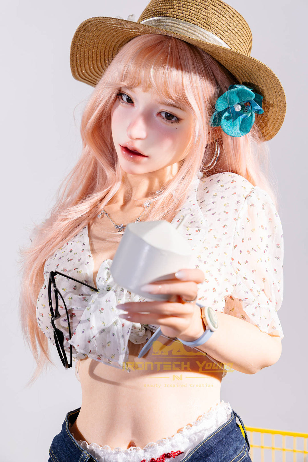 Irontech Doll 166 cm 2.0 Young Series E Silicone - Mio close-up holding a small item in both hands, straw sun hat, white top, playful pose