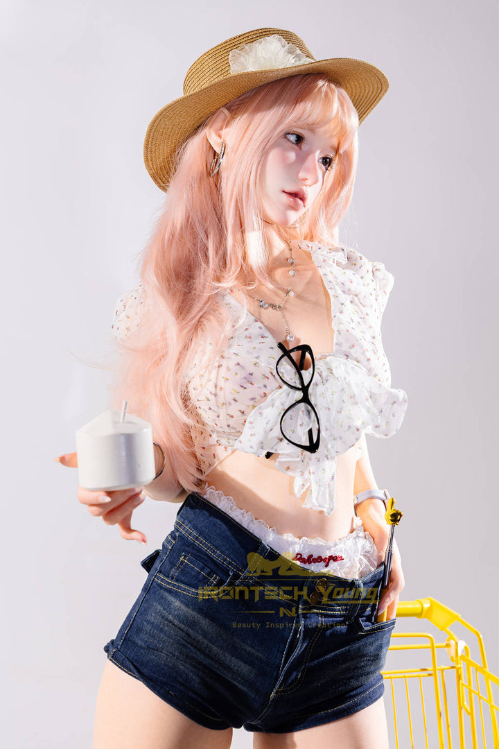 Irontech Doll 166 cm 2.0 Young Series E Silicone - Mio close-up kneeling beside a yellow roller-skate prop, straw sun hat with teal flower, white top