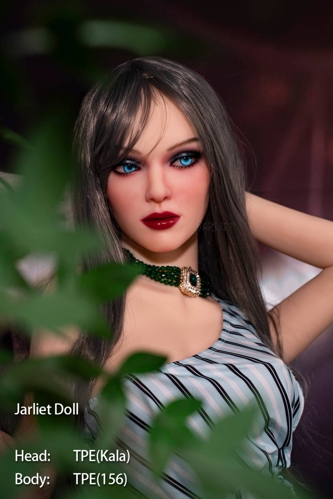 Jarliet Doll 156 cm B TPE - Kala V2 close-up portrait, dark straight hair with bangs, bold blue eyeshadow, red lips, black choker with pendant, black-and-white striped playsuit, hand raised near her hair, green foliage in the foreground, warm stadium lights in the background