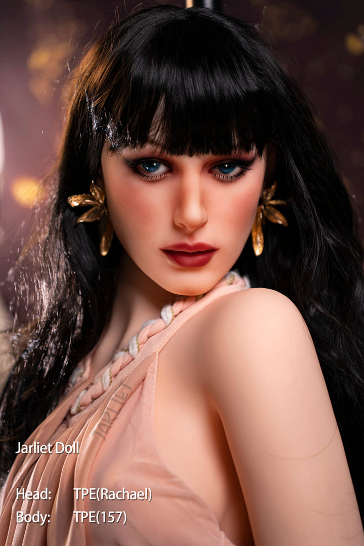 Jarliet Doll 157 cm B TPE - Rachael close-up portrait, long black wavy hair with bangs, dramatic blue eyeshadow, red lips, gold dangling earrings, beaded choker, peach satin slip dress, warm golden fantasy-forest backdrop