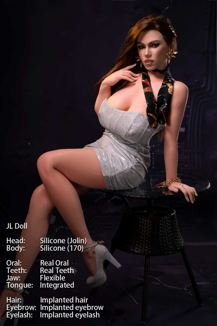 Jarliet Doll 170 cm G Silicone - Jolin wearing a sexy silver mini dress and heels, seated pose on side table, dark blue industrial background.