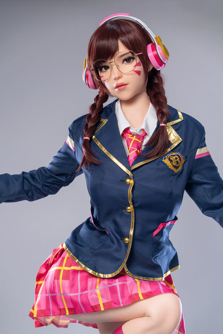 Game Lady 166 cm E Silicone – D.Va sitting while posing confidently, wearing a blue jacket and pink plaid skirt, showcasing her realistic silicone body and anime-inspired look.
