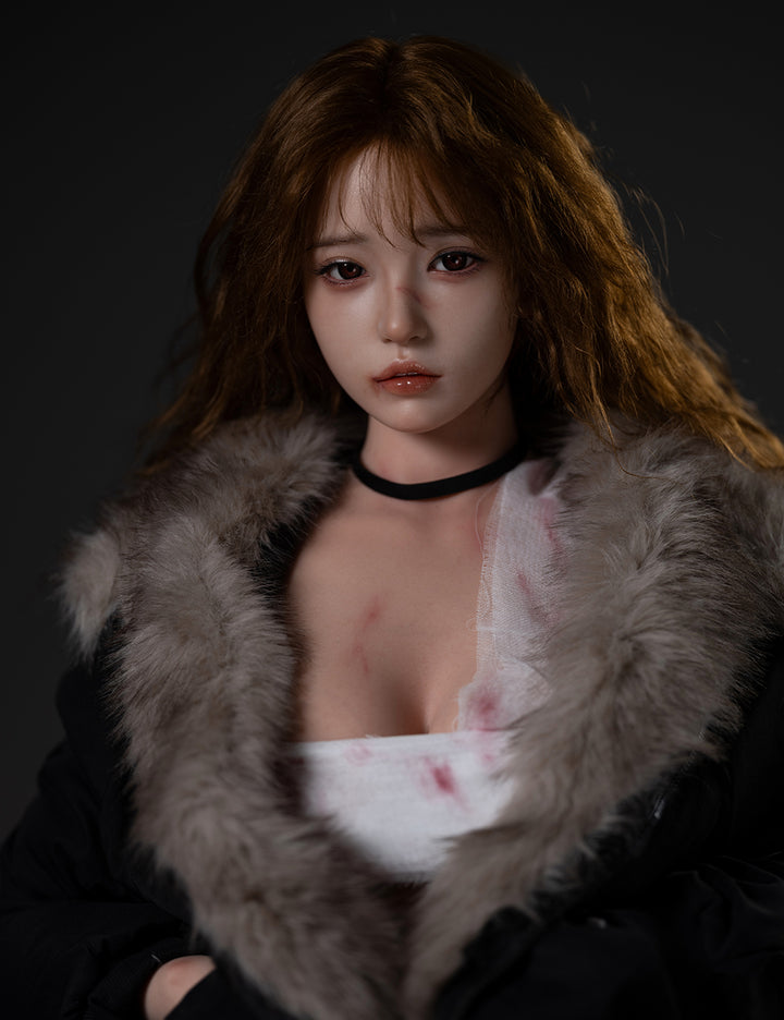 A close-up portrait of the TOP-CYDOLL 162cm E-Cup Liang Realistic Sex Doll featuring a realistic facial expression with light bruising, long wavy brown hair, and a fur-trimmed jacket.