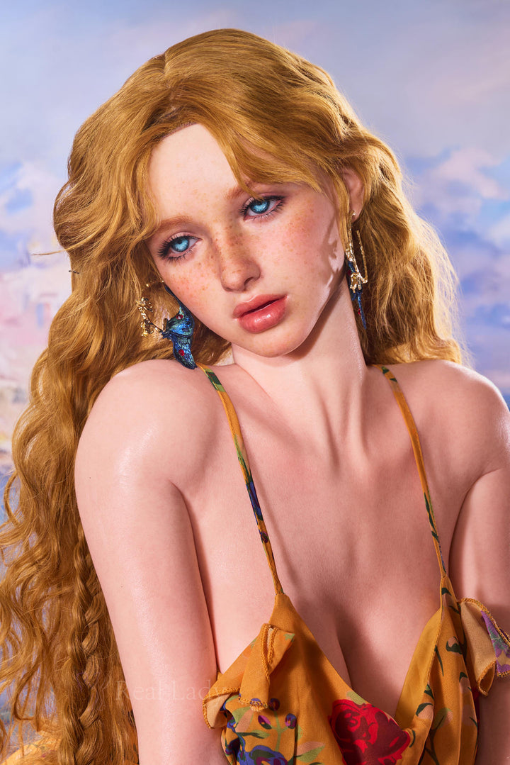 Close-up portrait of the RealLady 159 cm H Silicone - Elia featuring long wavy blonde hair, blue eyes, and freckles, wearing a yellow floral strap dress.