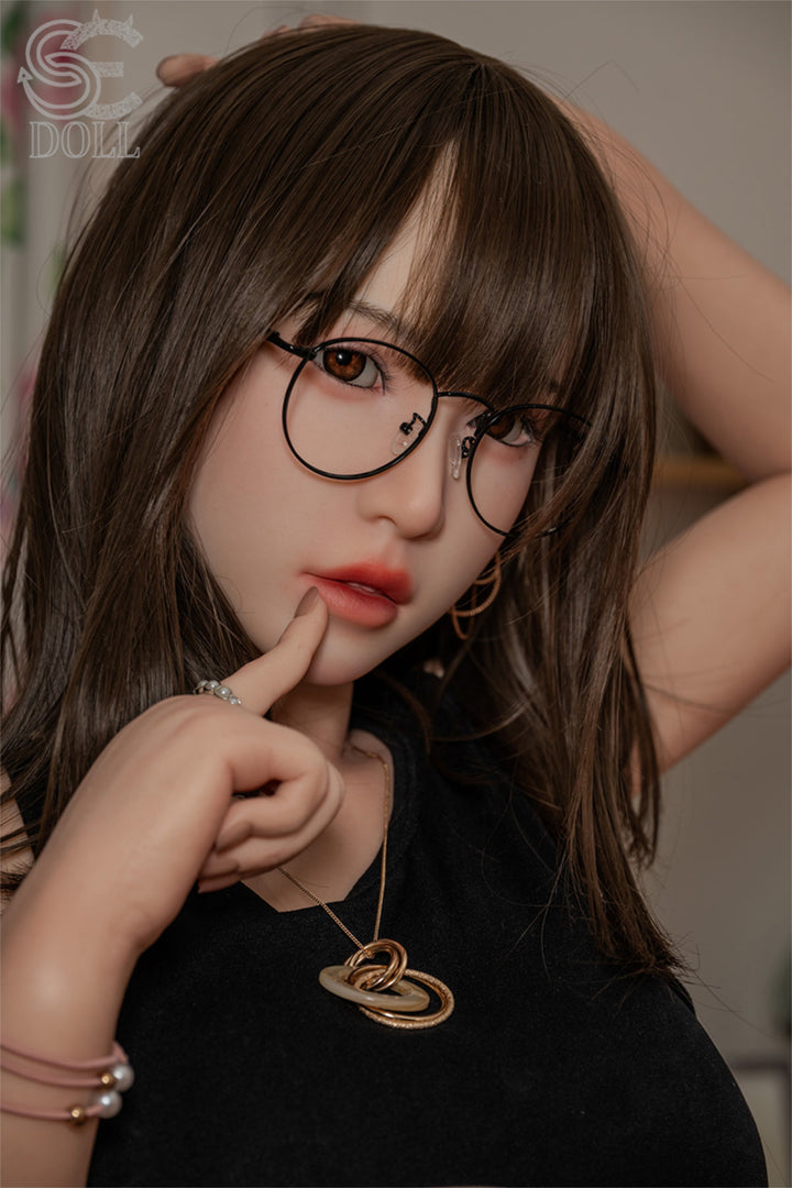 SEDOLL T153cm A Aya Series Silicone - Sena.A – Close-up pose adjusting eyeglasses, black cropped tank top, dark brown bangs framing the face, bedroom backdrop.