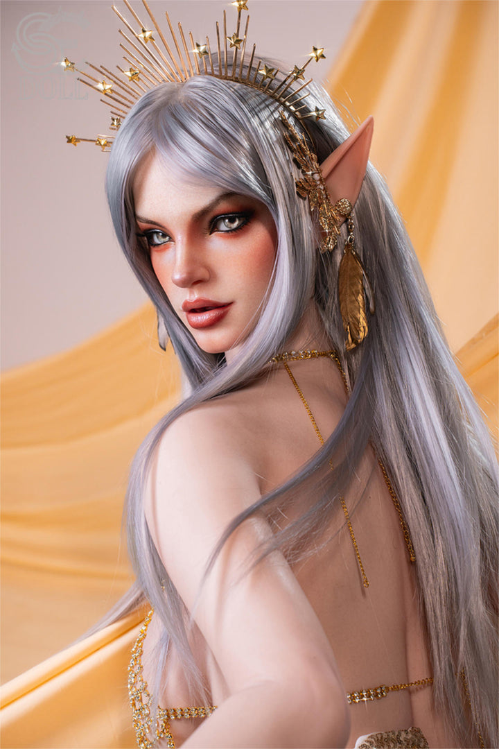 SEDOLL T167 cm E Silicone Pro - Evadora.A close-up with arms crossed over her chest, gold sequined dress catching the light, silver spiked headpiece, soft gaze toward camera