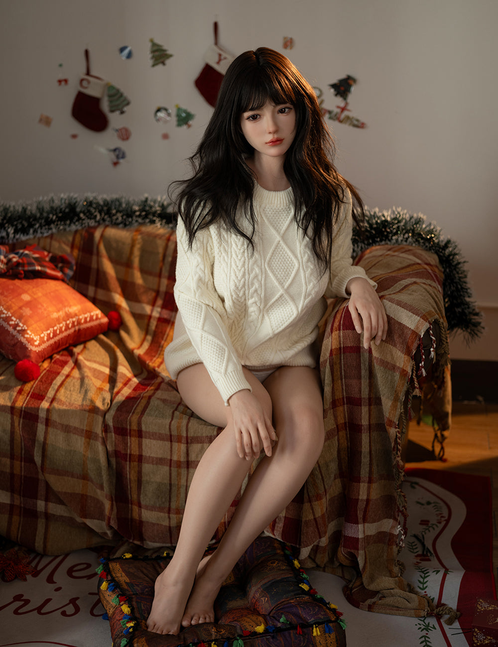 Full-body view of the TOP-CYDOLL 162 cm E-Cup Sato Asuka seated on a plaid-covered sofa in a festive setting, wearing a white cable-knit sweater.