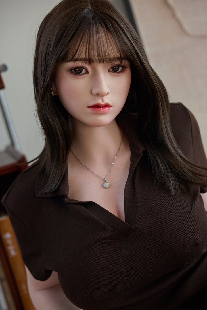 Starpery 154cm E - Yuan – Close-up seated pose, deep brown V-neck short-sleeve top with delicate pendant necklace, straight-cut dark bangs framing the face with hair falling past the shoulders, warm wooden interior backdrop.