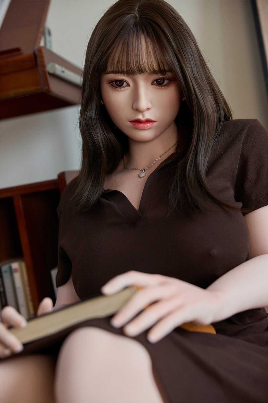 Starpery 154cm E - Yuan – Seated pose at a wooden table, brown V-neck top with buttoned front, holding a small object in one hand, dark straight-bang hairstyle, rustic wood-toned backdrop.