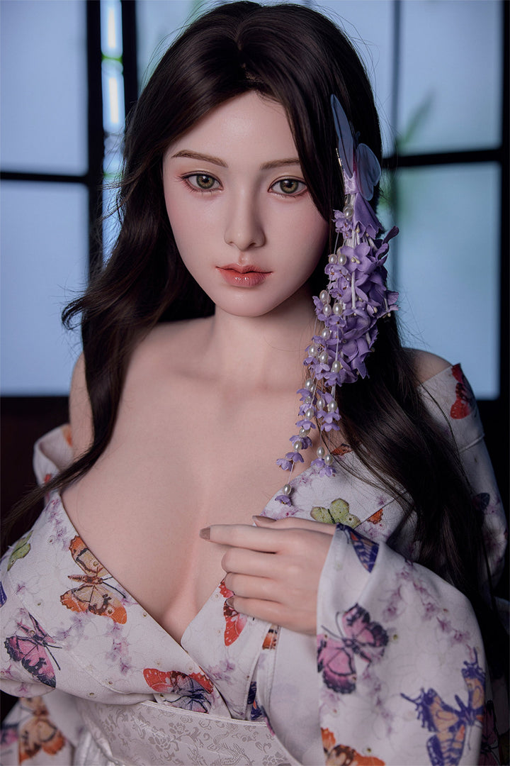 Starpery 171cm D - Xue V3 – Close-up seated pose, floral kimono-style robe open at chest, purple flowers in dark wavy hair, window backdrop.