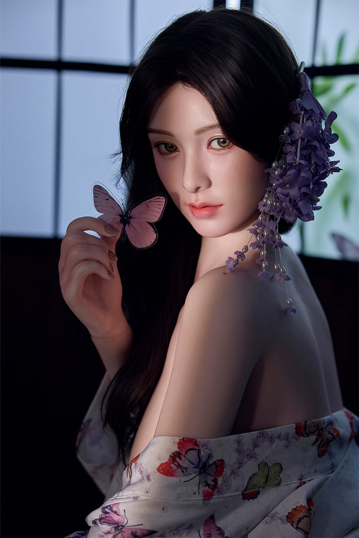Starpery 171cm D - Xue V3 – Seated side pose, floral kimono-style robe draped off shoulder, purple flowers in dark wavy hair, dark backdrop.