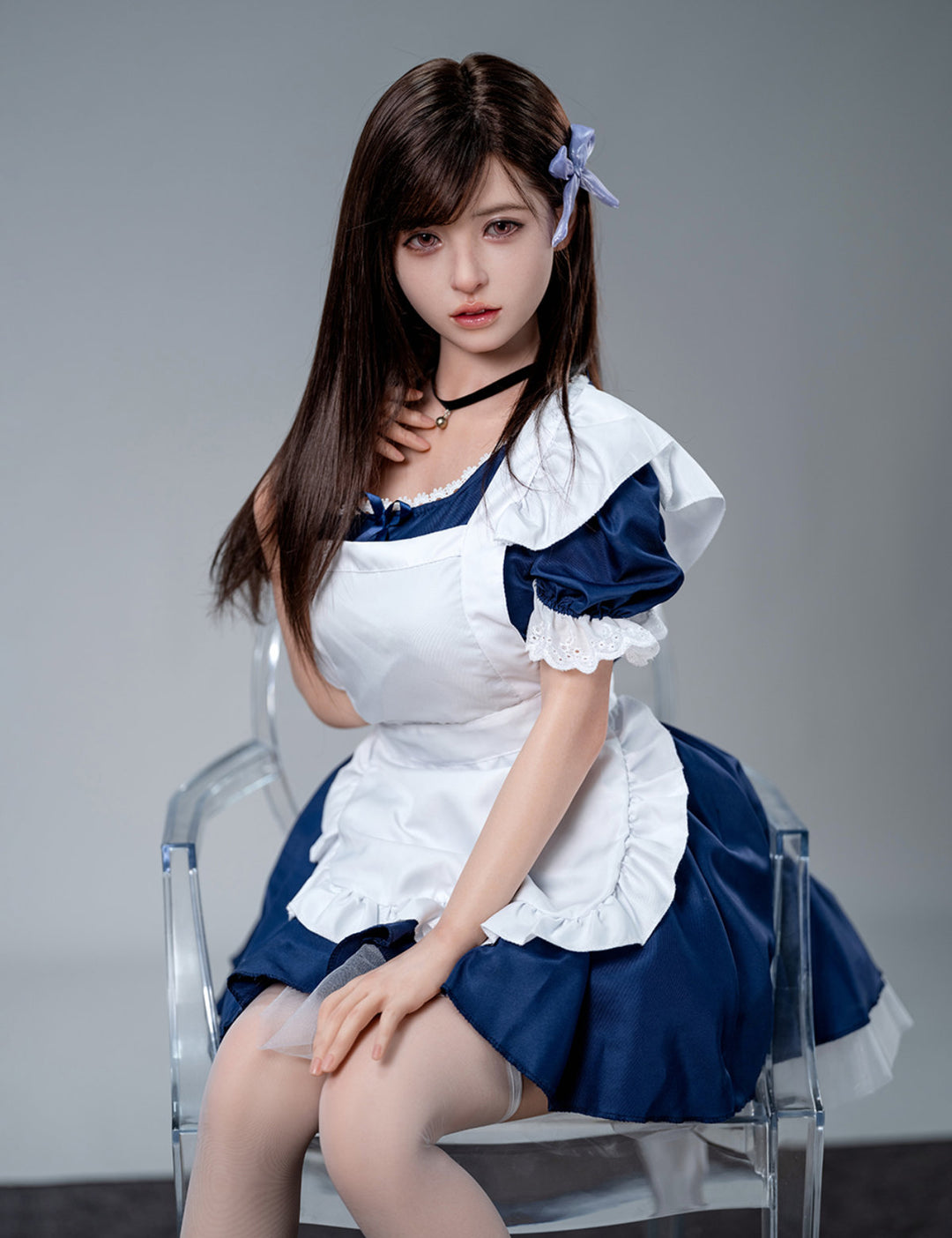 Seated view of the Koharu doll in a maid costume on a clear acrylic chair, looking slightly away from the camera.