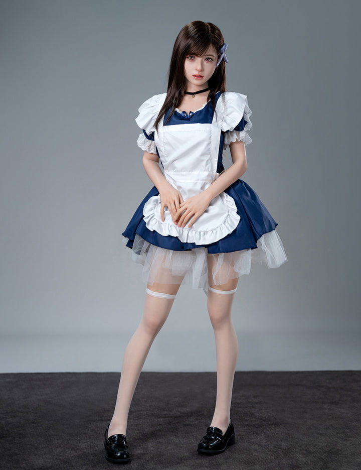 Full-body standing front view of the Koharu doll in a maid costume and white thigh-high stockings against a plain grey studio backdrop.