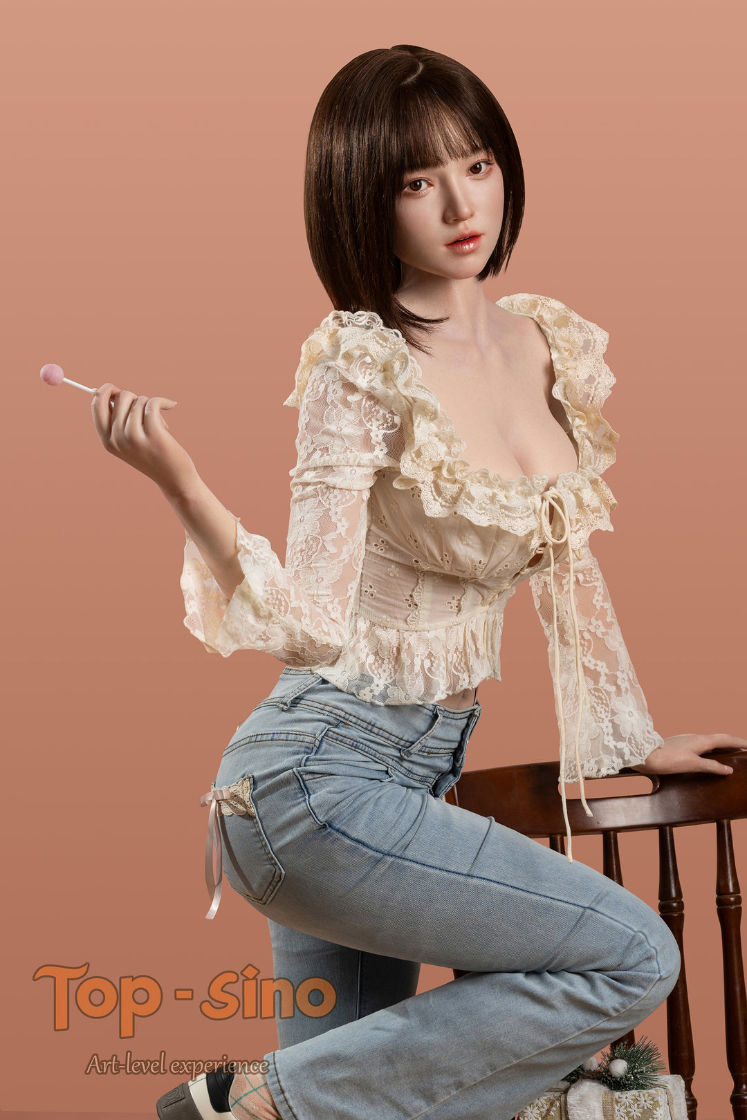 Top Sino 167 cm Platinum Silicone - Mimu (RRS+) - V2 wearing a beige floral lace top and blue jeans, holding a lollipop against a peach wall.