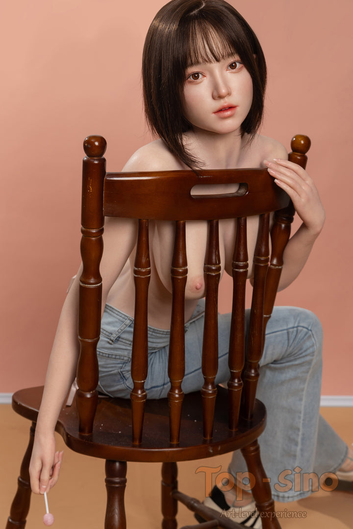 Top Sino 167 cm Platinum Silicone - Mimu (RRS+) - V2 sitting on a wooden chair wearing sexy denim shorts against a peach wall.