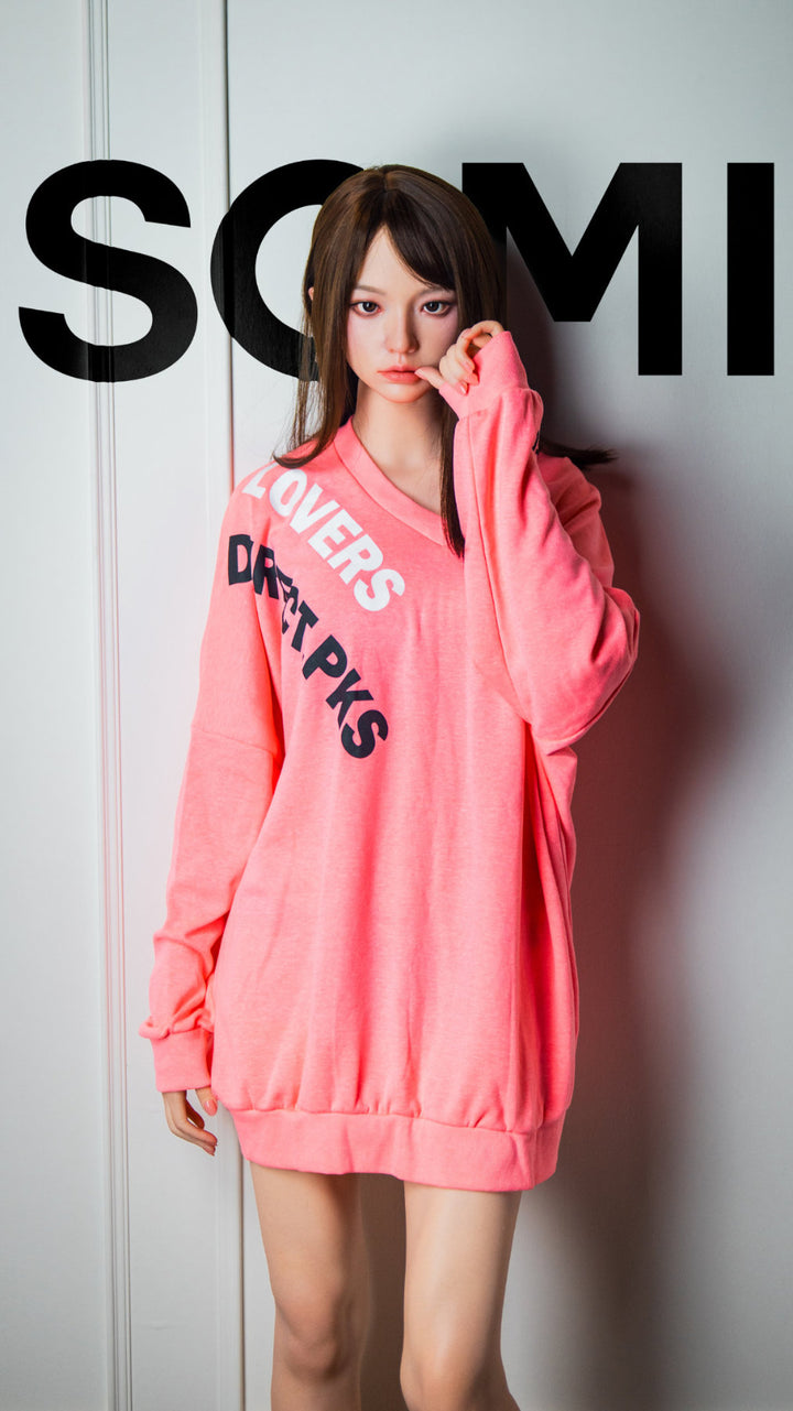 Zelex Doll K-Series 168 cm B Silicone - Somi full body standing pose in oversized pink hoodie with SOMI print, long dark brown hair, white studio background

