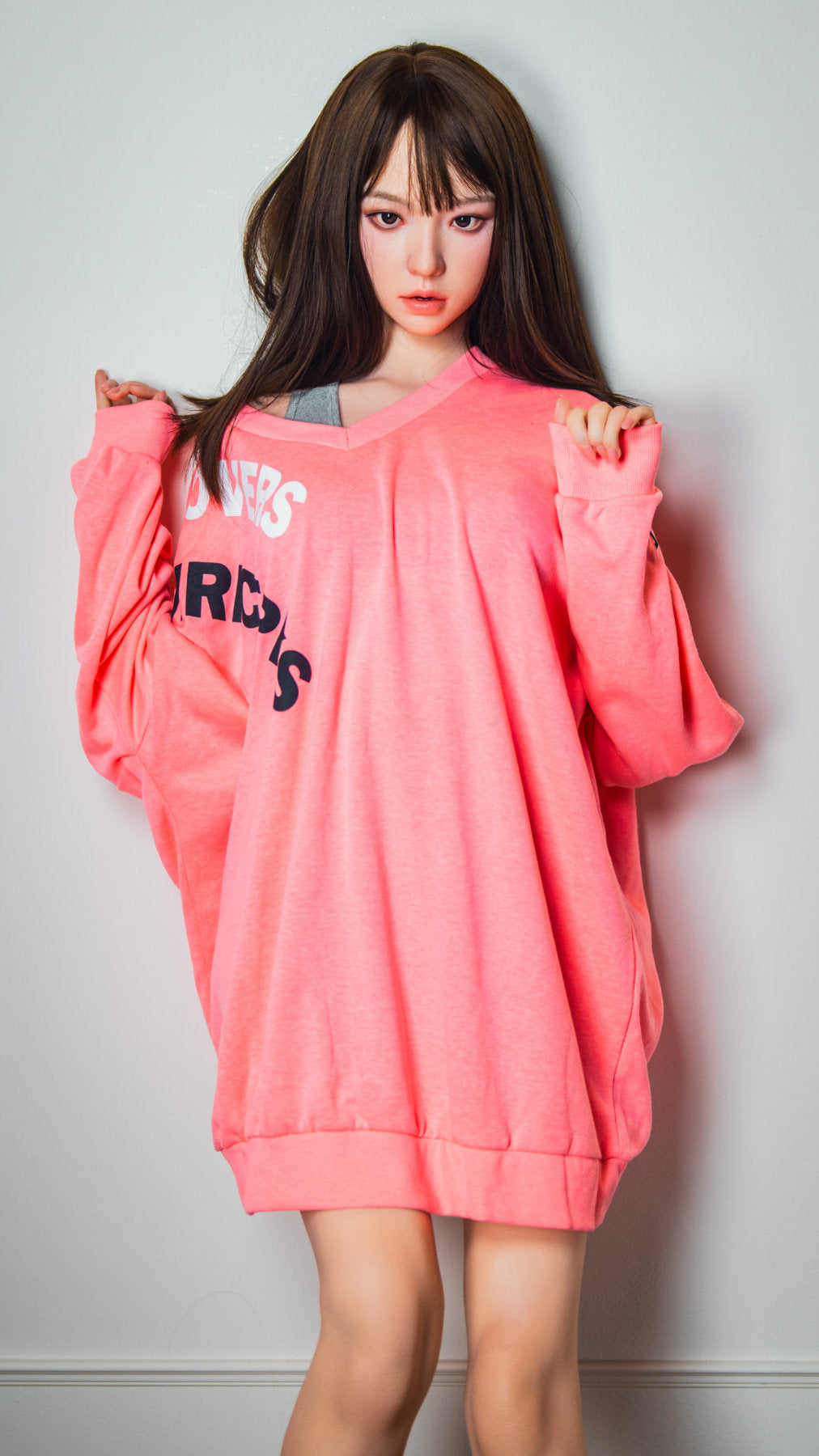Zelex Doll K-Series 168 cm B Silicone - Somi three-quarter view in oversized pink hoodie and blue denim shorts, long dark brown hair, white studio background

