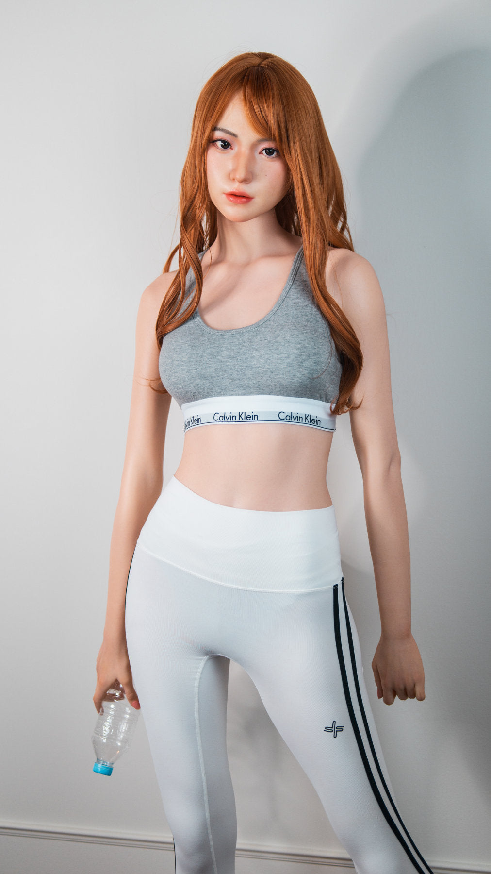 Zelex Doll K-Series 168 cm B Silicone - Suyeon three-quarter standing view in grey sports bra and white athletic leggings, long auburn hair, white studio background
